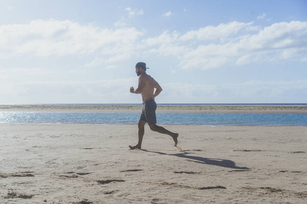 Бегущий мужчина бегает по пляжу. Мускулистый бегун тренируется на улице.
.