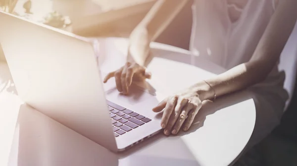 Gelukkig casual mooie vrouw die werkt op een laptop zitten aan de tafel in de woonkamer van moderne huis. Fakkels. — Stockfoto