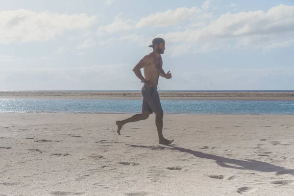 Corredor joven corriendo por la mañana a lo largo de la playa. Joven barbudo trotando en la orilla del mar al amanecer . —  Fotos de Stock