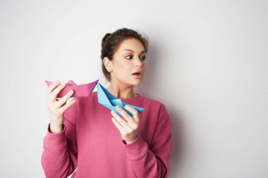 Bir iki mavi ve pembe renk kağıt gemi boş gri arka plan üzerinde tutan bir sürpriz kadın portresi. Duygu, insanlar, Güzellik, moda ve yaşam tarzı, seyahat, turizm ve kavram insanlar. Kopya hamur metin