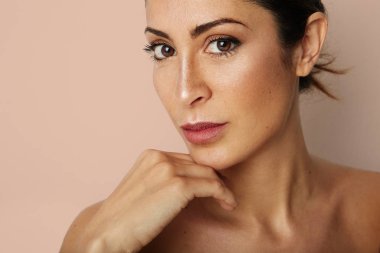 Güzellik kadını büyük kahverengi gözleri ve karanlık kaşları kameraya boş bej renkli arka plan üzerinde seyir. Işık çıplak makyaj ile model, stüdyo arka planını renklendirin, yapıştırma alanı kopyalayın, yakın çekim.