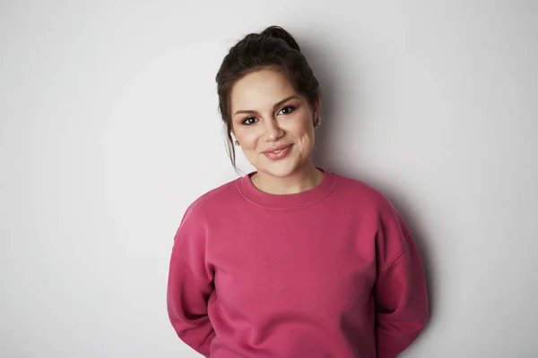 Young hipster girl wearing pink hoody with space for your logo or design. Mock-up of pink hoody on white empty wall in the background. — Stock Photo, Image