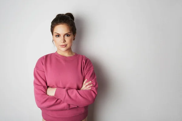 Beautiful hipster girl wearing pink hoody with space for your logo or design. Mock-up of pink hoody on white empty wall in the background. Copy paste text space. — Stock Photo, Image