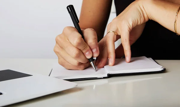 Belas mãos femininas escrevem caneta em um caderno de tarefas e objetivos para trabalhar em uma mesa de madeira.As mãos de uma mulher de negócios escrevendo em um bloco de notas com uma caneta . — Fotografia de Stock