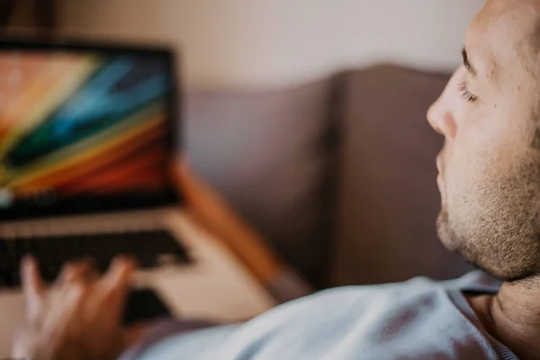 Arbeta stunder hemma. Unga kaukasiska medarbetare mannen i casual kläder arbetar på laptop på soffa på modern apartment. Suddig bakgrund. — Stockfoto