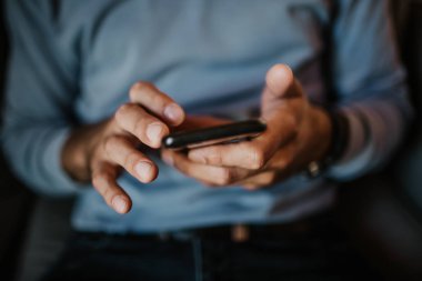 Erkek el smartphone tutarak yakından görünümü. Arka plan bulanık. Blogger mobil gadget'ı kullanma. Horizontal.Colors profili.