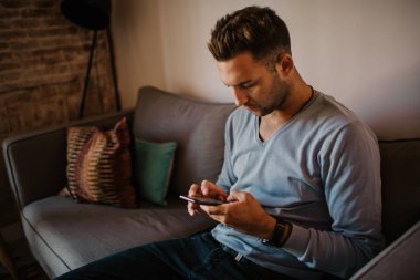 Yakışıklı adam için dalga köpüğü hareket eden smartphone kullanarak web internet ve gönderen sesli mesaj. Adam modern daire Gadget'ı kullanma.