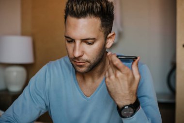 Yakışıklı adam için dalga köpüğü hareket eden smartphone kullanarak web internet ve gönderen sesli mesaj. Adam modern daire Gadget'ı kullanma.