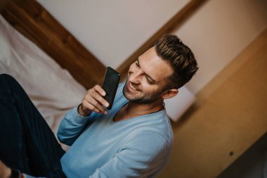 Yakışıklı adam için dalga köpüğü hareket eden smartphone kullanarak web internet ve gönderen sesli mesaj. Adam modern daire Gadget'ı kullanma.