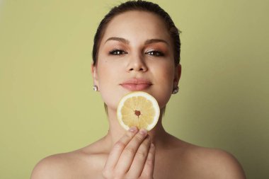 Kahverengi gözleri ve karanlık kaşları tutan güzel kadınlarla taze limon yakın renkli arka plan üzerinde dudaklarını uzat. Hafif makyaj çıplak, renk stüdyo arka plan modeli. Sağlık vücut kavramı.