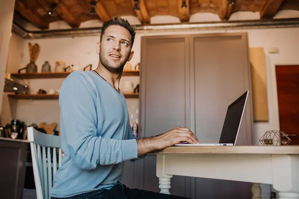 Arbeta stunder hemma. Unga kaukasiska medarbetare mannen i casual kläder arbetar på laptop på modern apartment. Suddig bakgrund. — Stockfoto