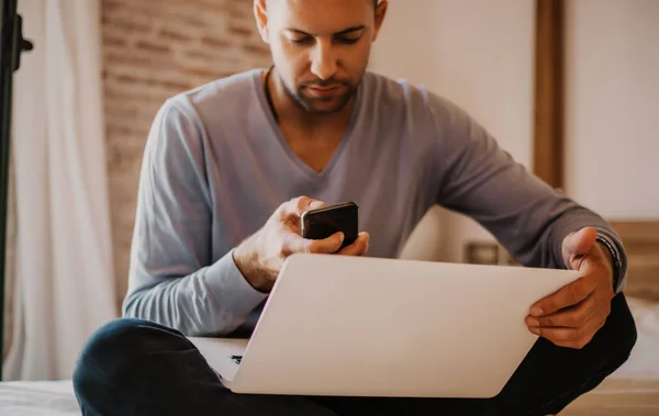 Arbeta stunder hemma. Unga kaukasiska medarbetare mannen i casual kläder arbetar på laptop på modern apartment. Suddig bakgrund. — Stockfoto