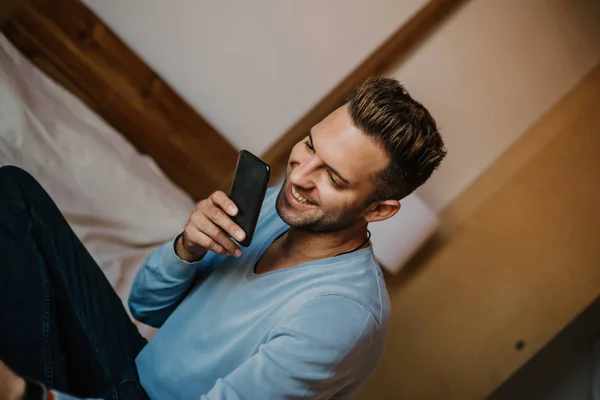 Bonito homem usando smartphone móvel para navegar na internet e enviar mensagem de áudio. Homem usando gadget no apartamento moderno . — Fotografia de Stock