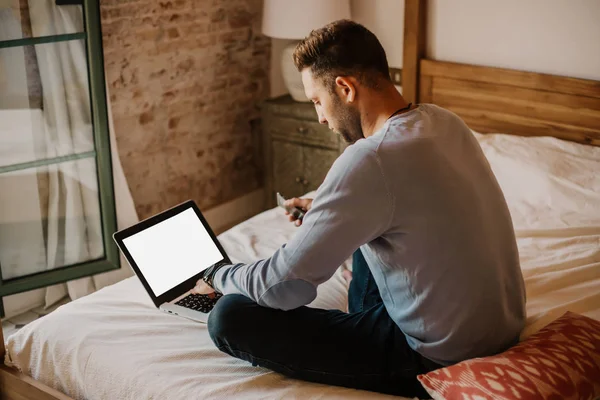 Arbeta stunder hemma. Unga kaukasiska medarbetare mannen i casual kläder arbetar på laptop på modern apartment. Suddig bakgrund. Mockup. — Stockfoto
