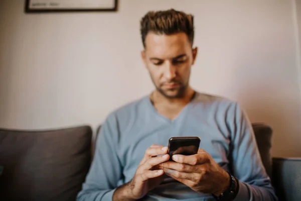 Bonito homem usando smartphone móvel para navegar na internet e enviar mensagem de áudio. Homem usando gadget no apartamento moderno . — Fotografia de Stock