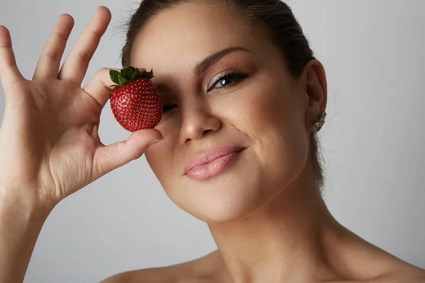 Ritratto di belle giovani donne sorridenti e tenendo la mano fragola fresca chiudere gli occhi su sfondo grigio.Modello con frutta su sfondo grigio studio. Primo piano . — Foto Stock