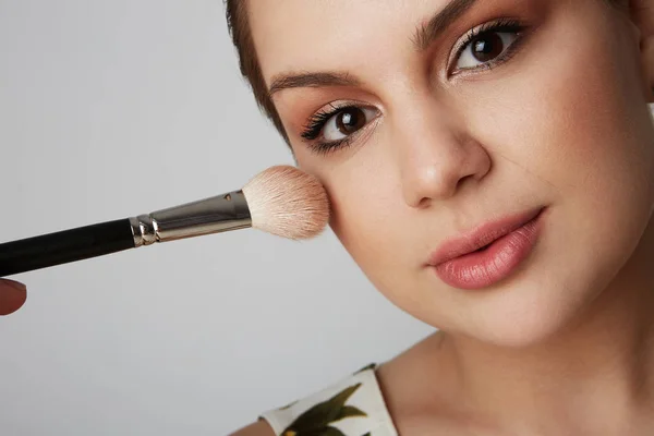 Schönes Mädchen mit braunen Haaren, sauberer, frischer Haut und einem kosmetischen Reinigungsgesicht, das vor grauem Studiohintergrund posiert, ein Model mit leichtem Nude-Make-up. — Stockfoto