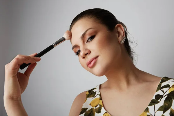 Schöne Mädchen mit schwarzen festen Haaren hinten, dunklen großen Augen, dicken Augenbrauen und Sommerkleid Make-up mit Mascara.model mit leichtem Nude-Make-up, Porträt über grauem Hintergrund. — Stockfoto