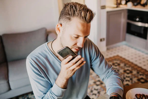 Bonito colega de trabalho a trabalhar na sala de estar em casa. Homem sentado à mesa de madeira usando laptop e telefone celular. Fundo desfocado . — Fotografia de Stock