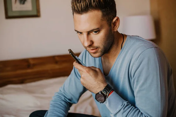 Werkende momenten thuis. De man van de jonge Kaukasische hipster in casual kleding bezig met laptop bij moderne appartement in slaapkamer. Onscherpe achtergrond. — Stockfoto