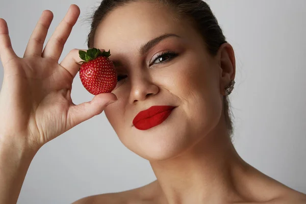 Portrait of handsome young women smiling and holding hand fresh strawberry close her eyes over gray background.Model with fruit and red lips over gray studio background. Closeup. — Stock Photo, Image