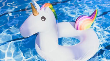 Şişme renkli beyaz tek boynuzlu at yüzme havuzunda. Plastik oyuncaklar yüzme havuzuyla tatil zamanında. Rahatlama ve eğlence kavramı. Güneş yansıması ile yüzme havuzunda su dalgalanma.