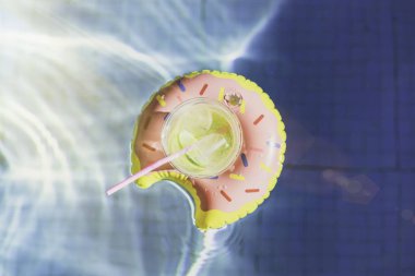 Buz ve şişme çörek oyuncak yüzme havuzunda üzerinde taze limon ile lezzetli kokteyl. Tatil ve dinlenme yaz günü, yüzme havuzunda. Güneş ışığı etkisi ve Ripple su yansıma.