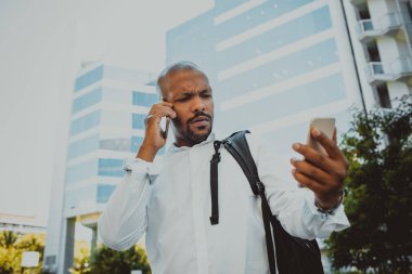 İki cep telefonu açık kullanarak pozitif Afro-Amerikan erkek. Office gökdelenler içinde belgili tanımlık geçmiş. İş stresi ve zor iş kavramı.