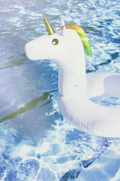 Unicornio blanco colorido inflable en la piscina. Tiempo de vacaciones en la piscina con juguetes de plástico.Ripple Agua en la piscina con reflejo solar.Sunlights efectos. Vertical . —  Fotos de Stock