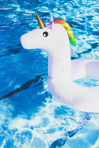 Unicornio blanco colorido inflable en la piscina. Tiempo de vacaciones en la piscina con juguetes de plástico. Relajación y concepto divertido. Ripple Agua en piscina con reflejo solar. Vertical . — Foto de Stock