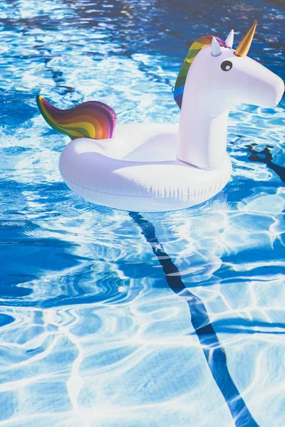 Unicorno bianco colorato gonfiabile alla piscina. Tempo di vacanza in piscina con giocattoli di plastica. Relax e divertimento concetto. Ondulazione Acqua in piscina con riflesso solare. Verticale . — Foto Stock