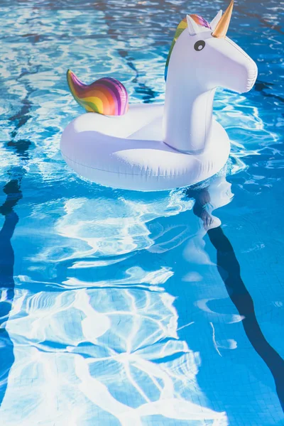 Надувні барвисті білий єдиноріг біля басейну. Відпустка у басейні плавають з Пластмасові іграшки. Концепція релаксації і веселощів. Брижі води в басейні зі відображення сонця. Вертикаль. — стокове фото