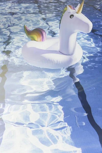 Надувний барвистий білий єдиноріг у басейні. Час відпустки в басейні з пластиковими іграшками. Ріплі Вода в басейні з відбиттям сонця. Ефекти сонячних променів. Вертикальний . — стокове фото