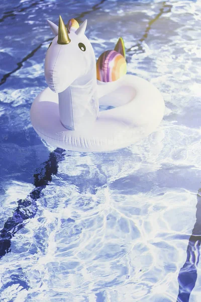 Надувний барвистий білий єдиноріг у басейні. Час відпустки в басейні з пластиковими іграшками. Ріплі Вода в басейні з відбиттям сонця. Ефекти сонячних променів. Вертикальний . — стокове фото