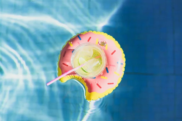 Свіжий коктейль з льодом і смачним лимоном, що плаває на надувній іграшковій рожевій пончиковій іграшці в басейні. . — стокове фото