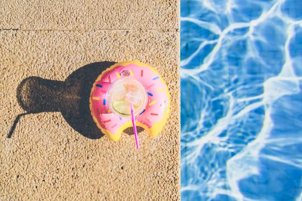 Смачний освіжаючий коктейль на надувній пончиковій пластиковій іграшці на краю басейну. Ріплі води в басейні з сонячним відображенням. Вид зверху . — стокове фото