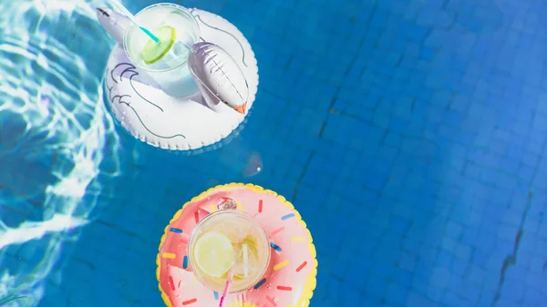Два свіжих коктейлі з льодом і смачним лимоном плавають на надувних іграшках білий фламінго і рожевий пончик іграшки в басейні. . — стокове фото