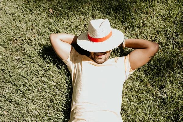 African-American male model laying in the green grass with trendy straw hat.African man hipster treveler relaxing at park. Leisure and rest at summer day.