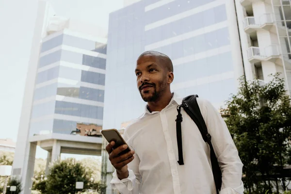 Positiv afrikanisch-amerikanischer Rüde mit Smartphone im Freien. Bürohochhäuser im Hintergrund. — Stockfoto