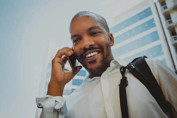 Positiv afrikanisch-amerikanischer Rüde mit Smartphone im Freien. Bürohochhäuser im Hintergrund. — Stockfoto