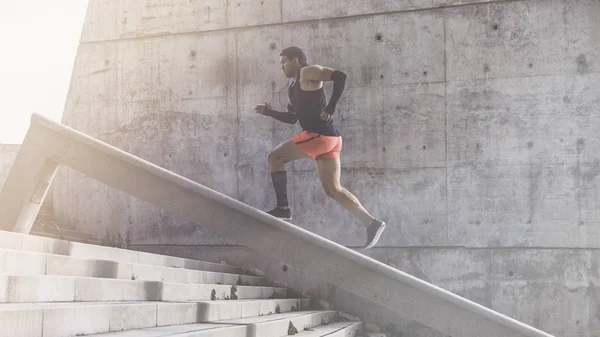 Musculoso hispano Joven atleta de piel oscura corriendo por un tramo de escaleras con velocidad, joven deportivo en entrenamiento de camiseta negra o haciendo ejercicio al aire libre mientras trota por los escalones. Bengalas . —  Fotos de Stock