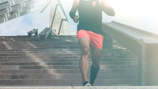Musculoso hispano Joven atleta de piel oscura corriendo por un tramo de escaleras con velocidad, joven deportivo en entrenamiento de camiseta negra o haciendo ejercicio al aire libre mientras trota por los escalones. Amplio . —  Fotos de Stock