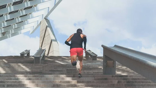Musculoso hispano Joven atleta de piel oscura corriendo por un tramo de escaleras con velocidad, joven deportivo en entrenamiento de camiseta negra o haciendo ejercicio al aire libre mientras trota por los escalones. Amplio . —  Fotos de Stock