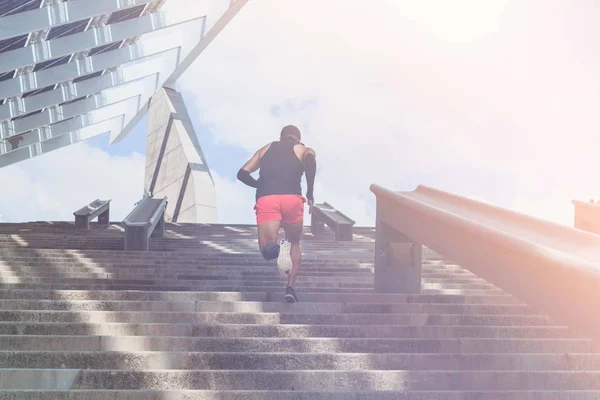 Musculoso hispano Joven atleta de piel oscura corriendo por un tramo de escaleras con velocidad, joven deportivo en entrenamiento de camiseta negra o haciendo ejercicio al aire libre mientras trota por los escalones. Bengalas . —  Fotos de Stock