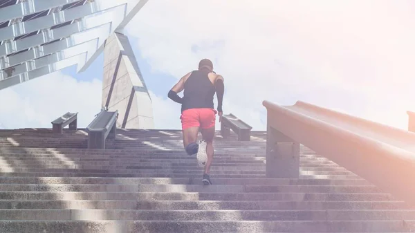 Musculoso hispano Joven atleta de piel oscura corriendo por un tramo de escaleras con velocidad, joven deportivo en entrenamiento de camiseta negra o haciendo ejercicio al aire libre mientras trota por los escalones. Flares.Wide . —  Fotos de Stock