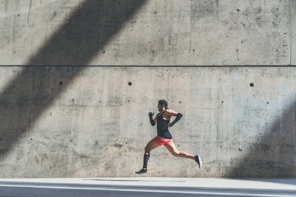 Deportista atleta masculino muscular corriendo rápido, ejercitándose al aire libre, trotando afuera contra fondo de concreto gris con área de espacio de copia para mensaje de texto o contenido publicitario. Vista lateral, longitud completa —  Fotos de Stock