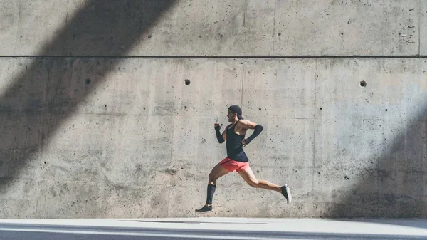 Deportista atleta masculino muscular corriendo rápido, haciendo ejercicio al aire libre, trotando afuera contra fondo de concreto gris con área de espacio de copia para mensaje de texto o contenido publicitario. Vista lateral, longitud completa. Amplio . —  Fotos de Stock