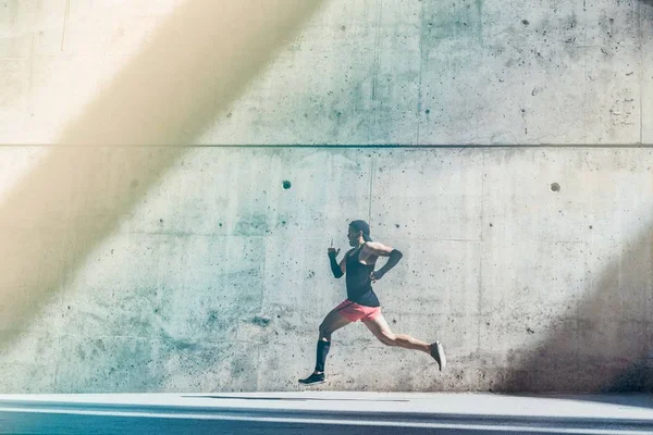 Deportista atleta masculino muscular corriendo rápido, ejercitándose al aire libre, trotando afuera contra fondo de concreto gris con área de espacio de copia para mensaje de texto o contenido del anuncio. Vista lateral, longitud completa. —  Fotos de Stock