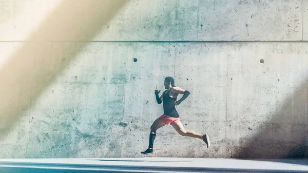 Deportista atleta masculino musculoso corriendo rápido, haciendo ejercicio al aire libre, trotando afuera contra fondo de concreto gris con área de espacio de copia para mensaje de texto o contenido del anuncio.Vista lateral, longitud completa.Amplio . —  Fotos de Stock