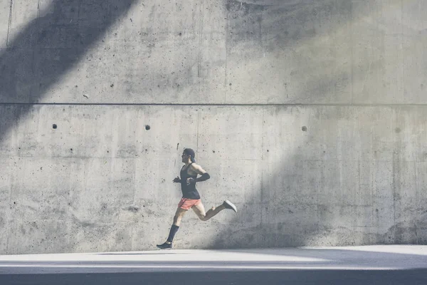 Deportista musculoso atleta velocista corriendo rápido, haciendo ejercicio al aire libre, trotando afuera contra fondo de hormigón gris con área de espacio de copia para mensaje de texto o contenido del anuncio.Vista lateral, longitud completa . —  Fotos de Stock
